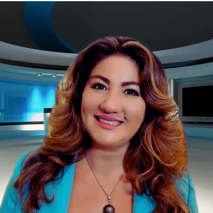 A woman with light brown/reddish hair, brown eyes, and a bright smile. She is wearing a black necklace and blue jacket.