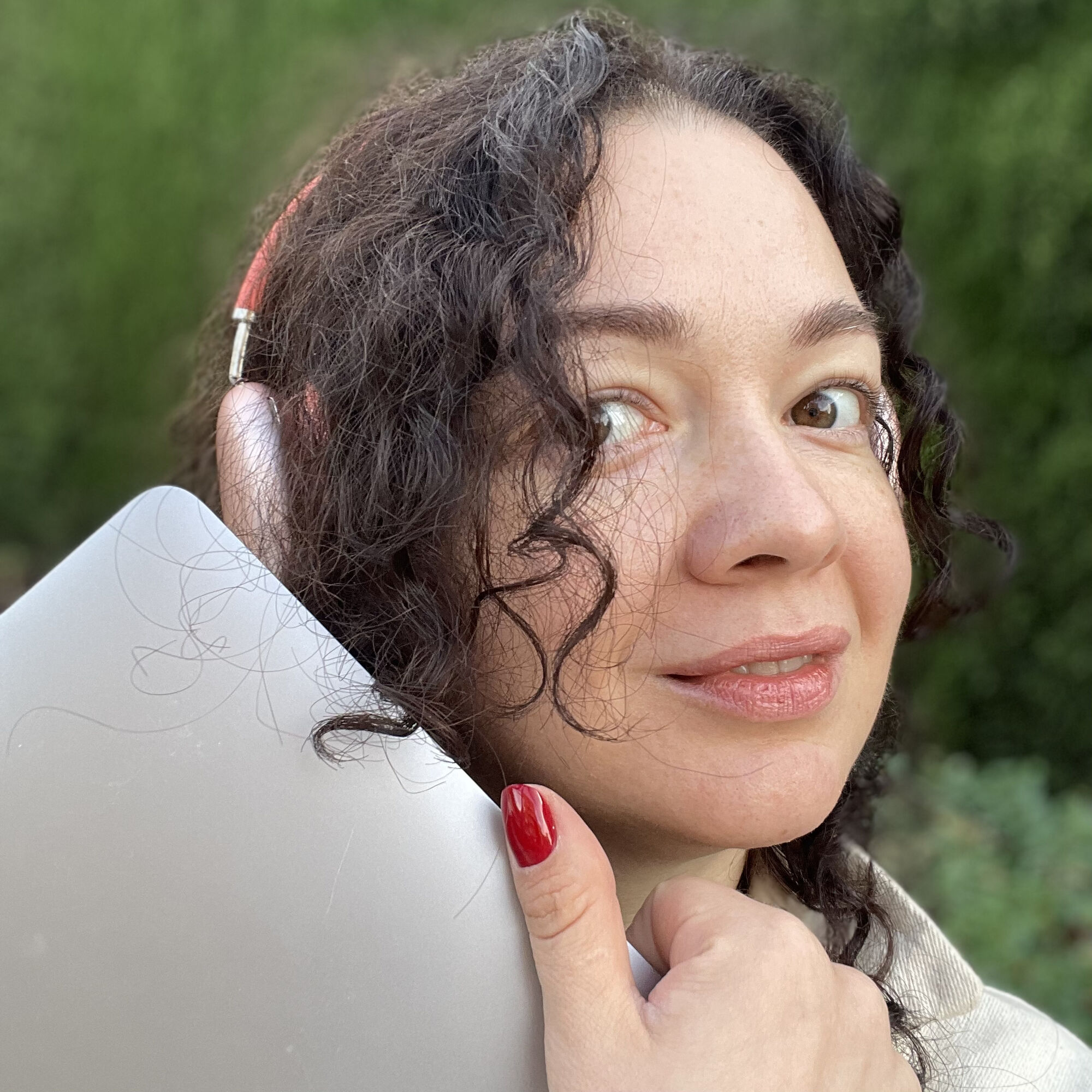 A woman with curly dark hair with a pink headphone, and carrying a laptop. 