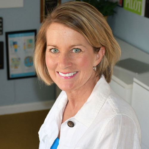 Tara Claeys - Women with blue eyes and blond hair in a bob style, smiling warmly. Wearing a white shirt. 