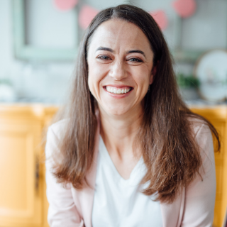Cheryl Hock is a slender woman with a wide smile, dark eyes, and dark hair. She is wearing a white shirt and pink jacket.