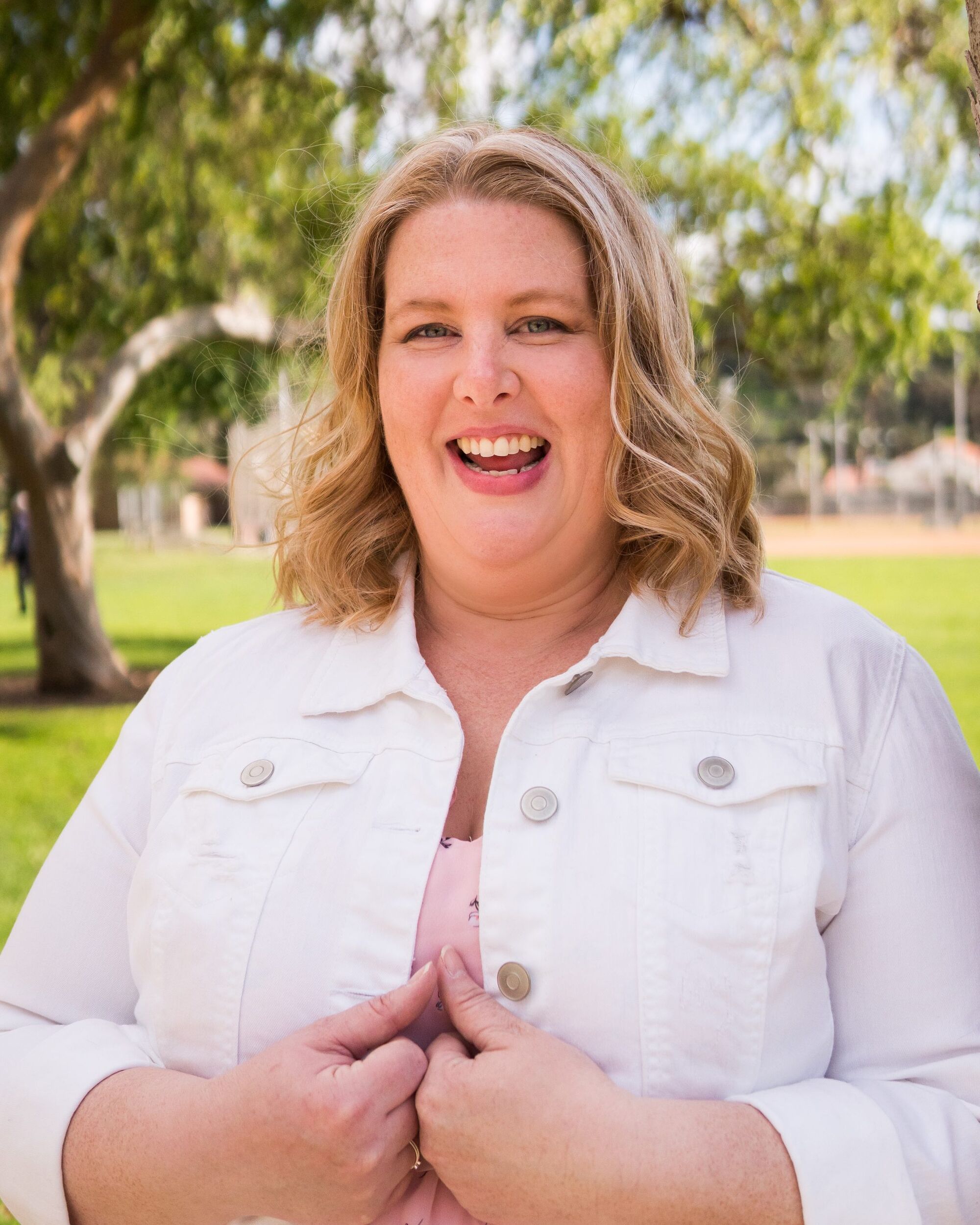 Portrait of Natalie Maclees, a smiling woman with short blonde hair, wearing a pink shirt under a white jacket.